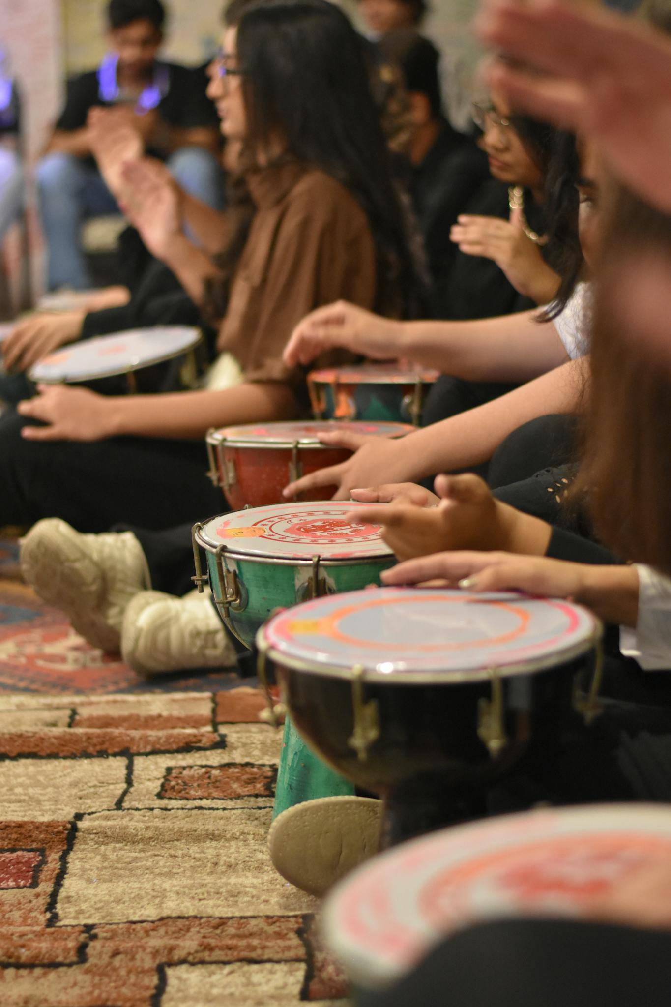 A group of young adults engaged in a lively indoor drumming circle, creating music together.