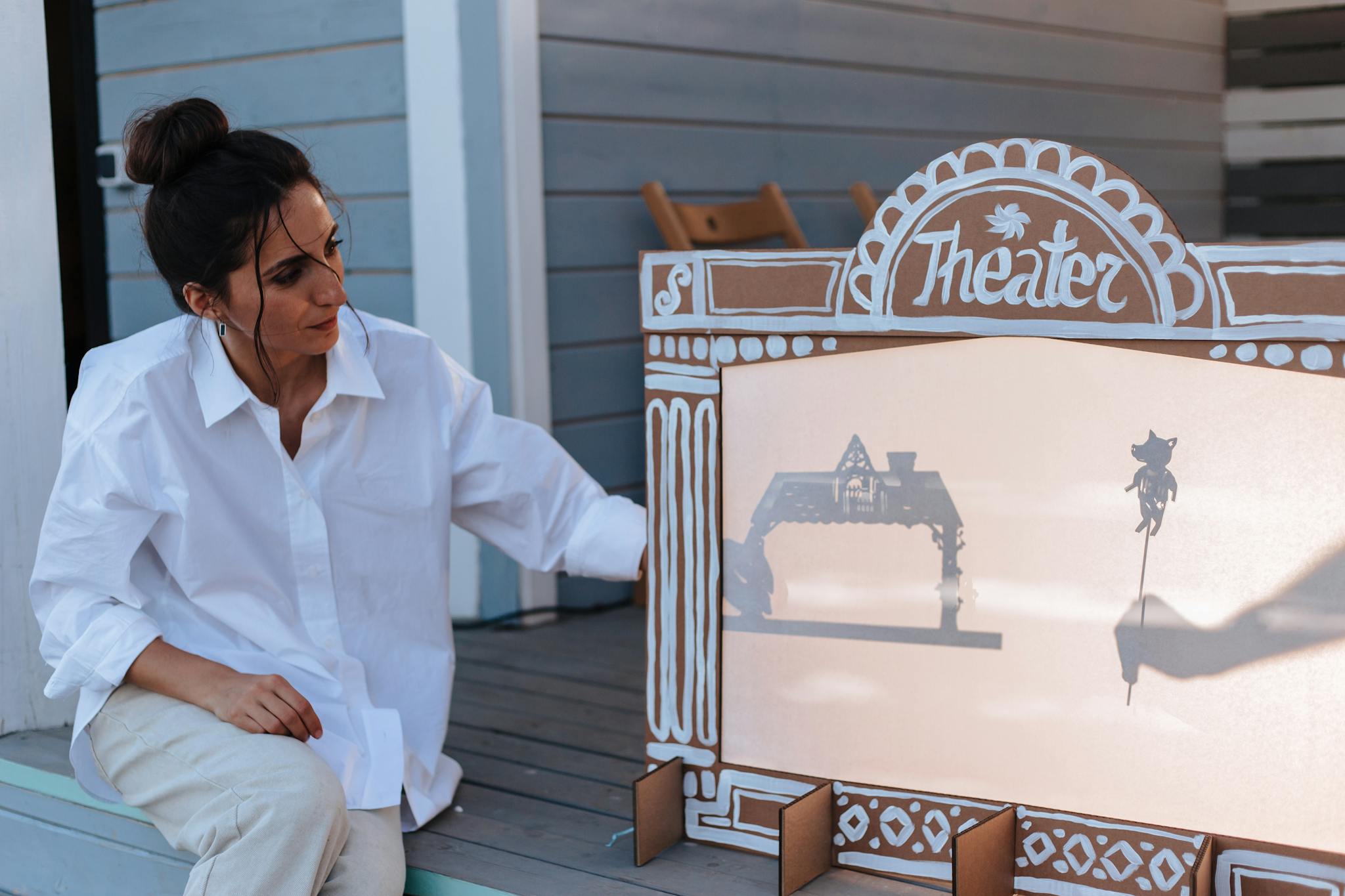 Woman interacts with a shadow puppet theater outdoors, showcasing creativity in storytelling.